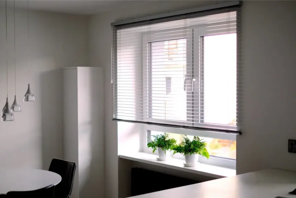 Weißes Kunststofffenster in der Küche mit Jalousien und Pflanzen. NORTA bietet moderne Lösungen für Wohnräume.