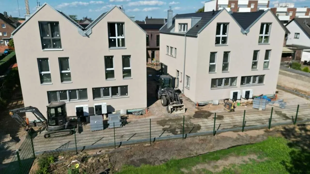 Bau eines modernen Doppelhauses in Köln. Fortschritte im Bauprozess, umgeben von Baumaterialien und Maschinen.