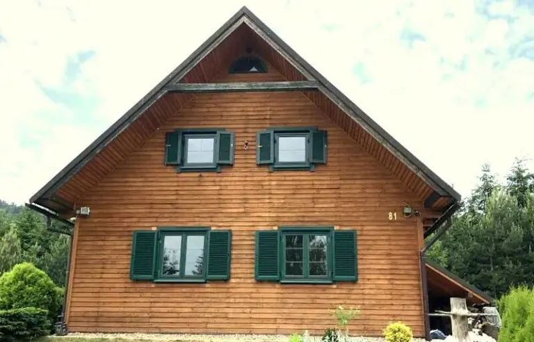 Holzhaus mit grünen Fensterläden aus Aluminium von NORTA, die für Eleganz und Witterungsbeständigkeit sorgen.