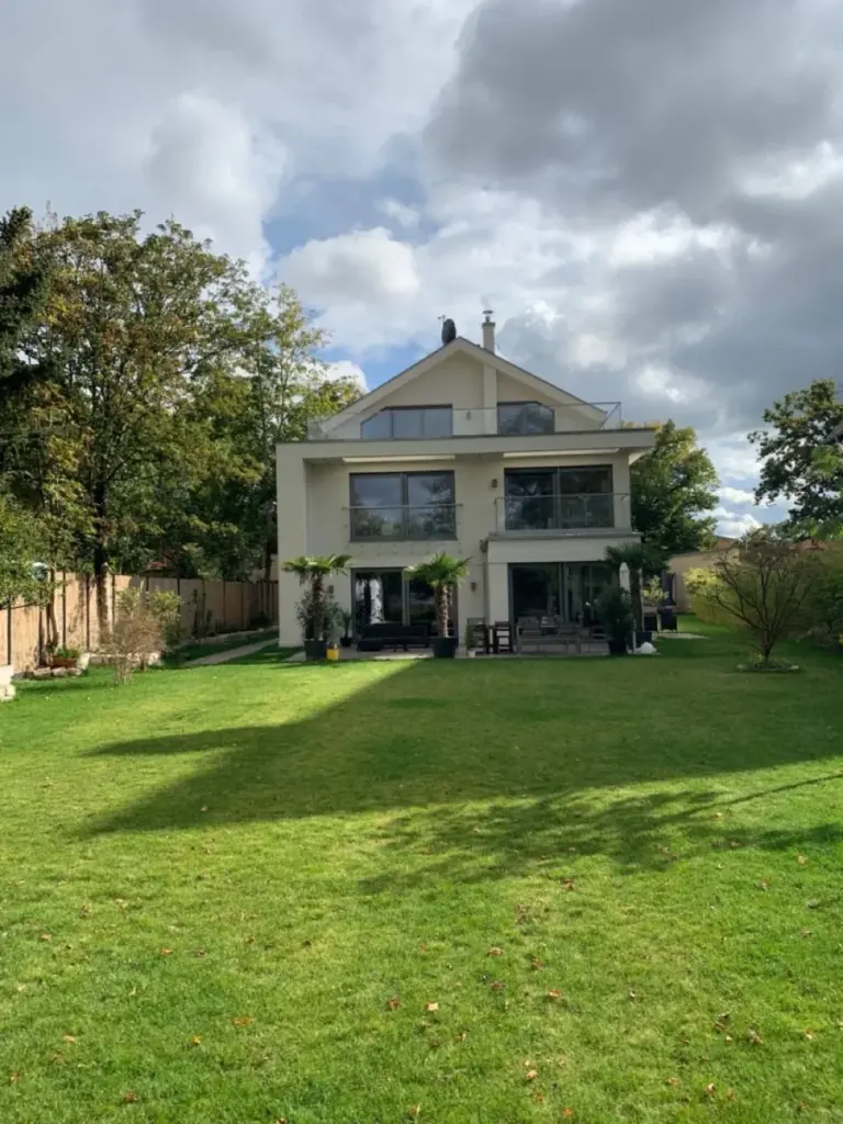 Modernes Einfamilienhaus mit großen Alufenstern von NORTA, umgeben von gepflegtem Garten und Bäumen, in Polen gelegen.