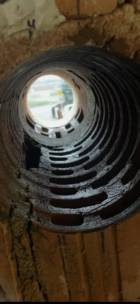 Blick durch eine frisch gebohrte, runde Kernbohrung in einer dicken Ziegelwand, die den Querschnitt der Mauersteine und den Ausblick nach draußen zeigt.
