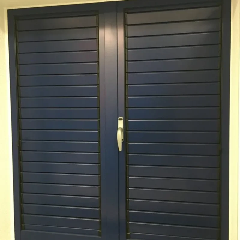 Aluminium-Fensterladen mit blauen Lamellen von NORTA. Robuste und stilvolle Lösung für Sichtschutz und Belüftung.