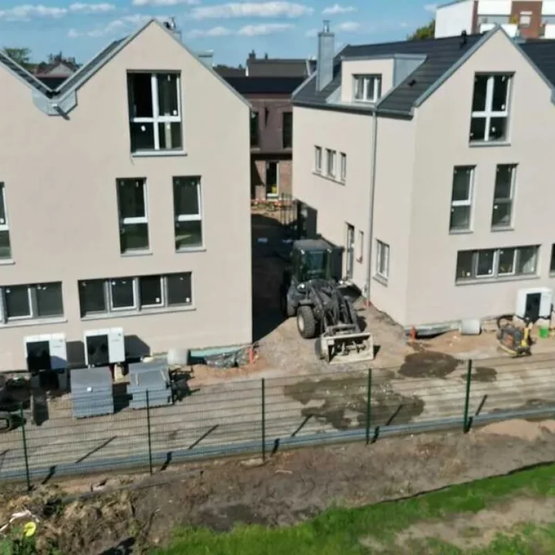 Bau eines modernen Doppelhauses in Köln. Fortschritte im Bauprozess, umgeben von Baumaterialien und Maschinen.