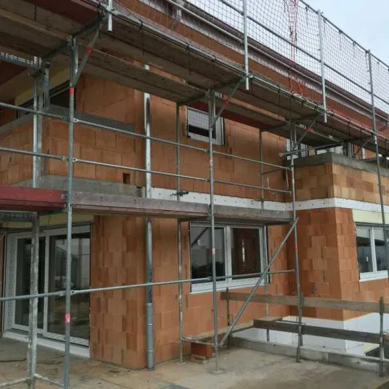 Baustelle eines Hauses mit Gerüst und eingebauten Fenstern von NORTA. Moderner Hausbau für hohe Energieeffizienz.