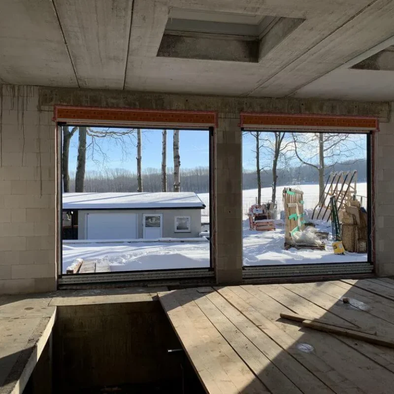 Großes Baustellenfenster im Rohbau mit Blick auf schneebedeckte Landschaft. Hochwertige Lösung von NORTA für klare Sicht und Energie.