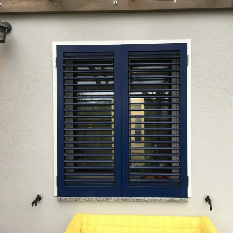 Blauer Aluminium-Fensterladen von NORTA. Robuste, wetterfeste Lösung für moderne Fensterästhetik bei hoher Funktionalität.
