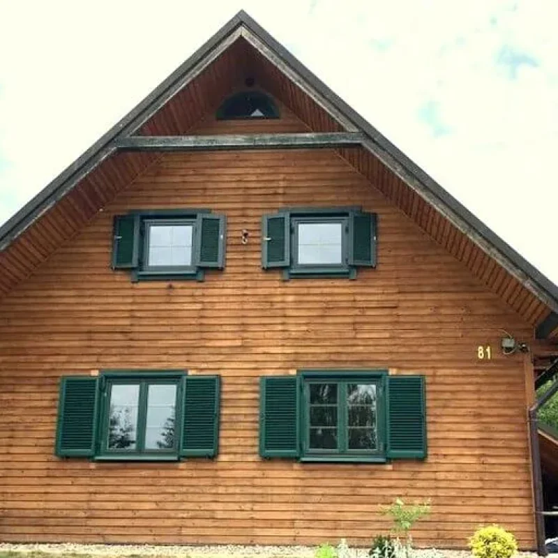Holzhaus mit grünen Fensterläden aus Aluminium von NORTA, die für Eleganz und Witterungsbeständigkeit sorgen.