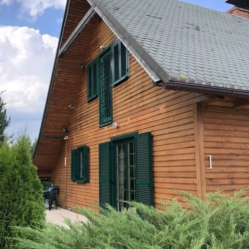Holzhaus mit grünen Fensterläden aus Aluminiumprofilen von NORTA. Hochwertiger Sichtschutz für ländliche Architektur.