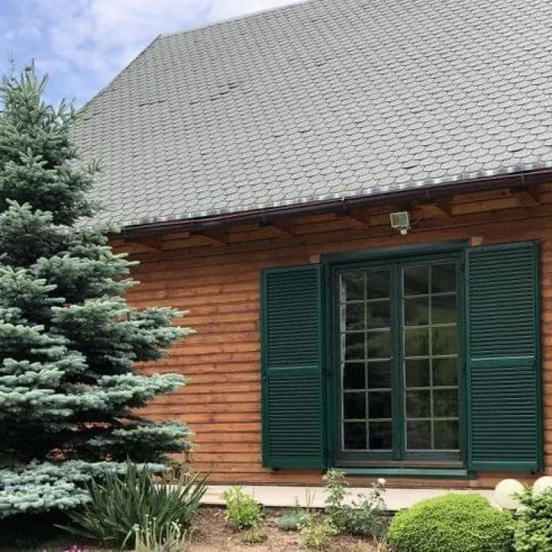 Aluminiumfensterläden in Grün an einem Holzhäuschen. Stilvolle und wetterfeste Lösung von NORTA für funktionalen Sonnenschutz.
