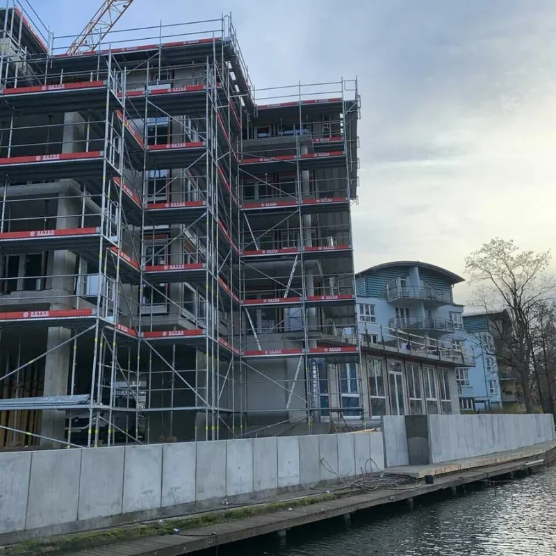 Gebäude mit Gerüst an einer Flussseite bei Sonnenuntergang. Modernes Bauprojekt mit transparenten Wänden von NORTA.