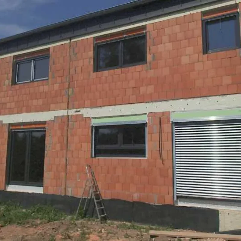 Haus im Bau mit großen Fenstern und installiertem Rollladen von NORTA. Robuste Bauweise für effektiven Sonnenschutz.