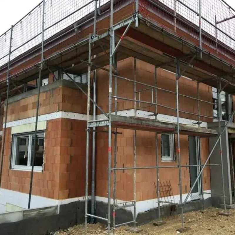 Hausbau mit Gerüst und Mauerwerk in Bauphase von NORTA. Solides Fundament für moderne, energieeffiziente Gebäude.