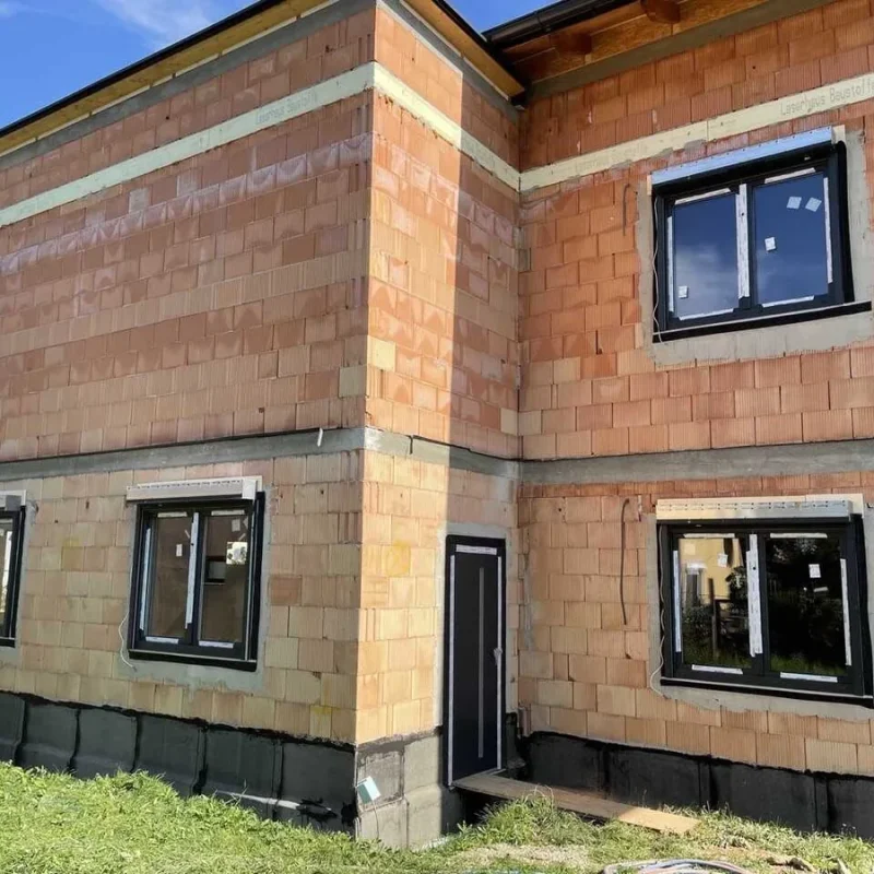 Rohbau eines Hauses mit Ziegelwänden und eingesetzten Fenstern von NORTA. Fortschrittlicher Bau für effektive Wärmedämmung.