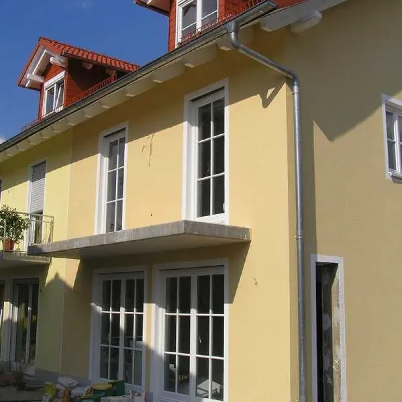 Holzfenster in gelber Fassade mit Dachfenstern von NORTA. Stilvolle Optik und hohe Wärmedämmung für Wohngebäude.