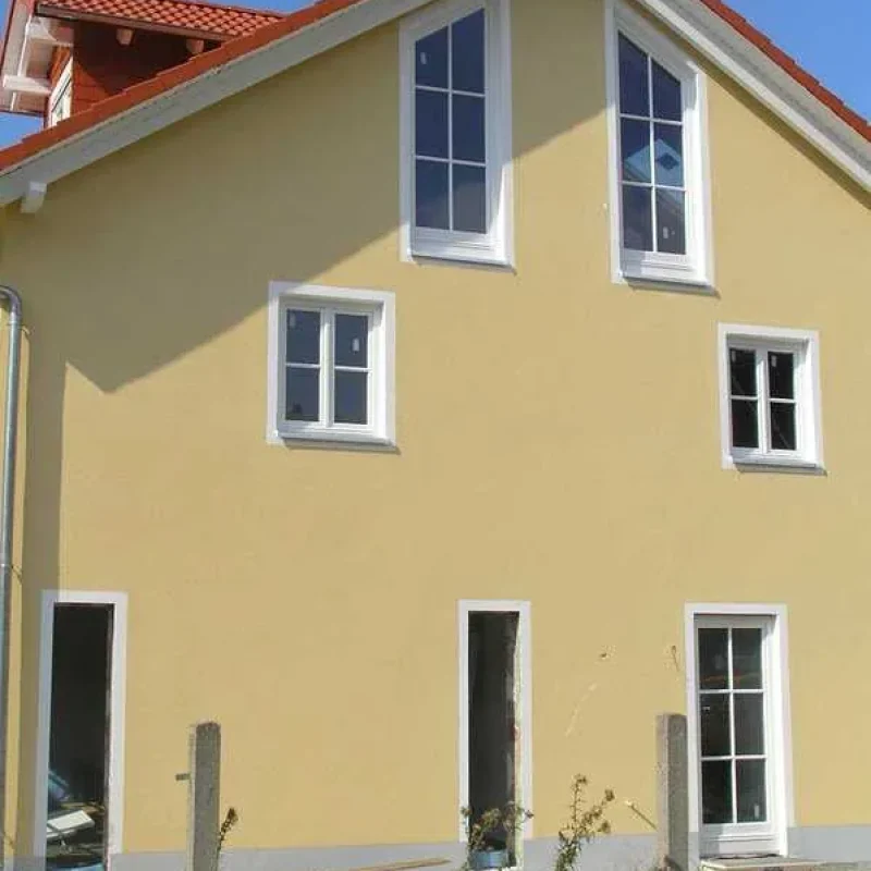 Gelbes Haus mit weißen Holzfenstern von NORTA. Stilvolle Fensterlösung für natürliches Licht und Wärmeisolierung.