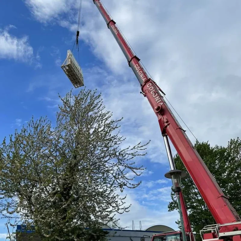 Großer roter Kran hebt Baumaterialien hoch. Effiziente Lösung für Baustellen in Köln von NORTA.