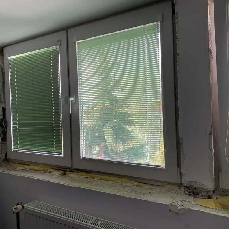 Kunststofffenster mit Pfosten und grünen Jalousien von NORTA. Verbessert die Lichtregulierung und Wärmedämmung im Raum.