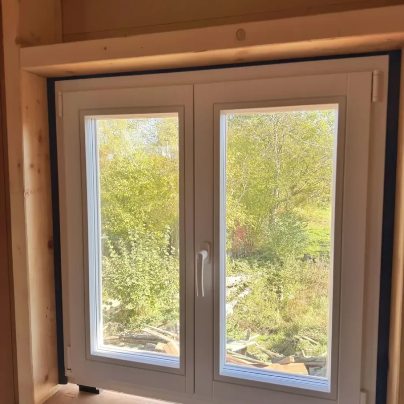 Weißes Kunststofffenster in einem Holzhaus von NORTA. Moderne Isolierung mit Blick in den Garten.