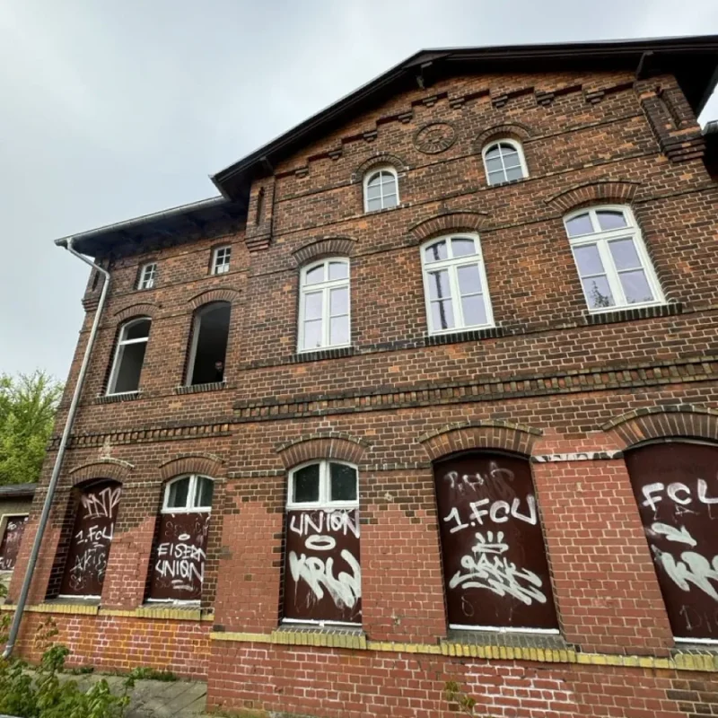 Backsteingebäude mit alten Holzfenstern, einige Fensteröffnungen mit Graffiti-beschmierten Platten geschlossen. NORTA inspiriertes Design.