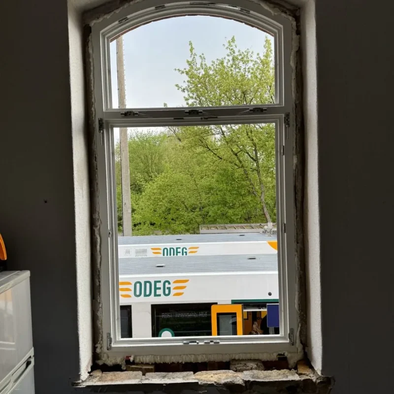 Holzfenster in Havelsee-Bauweise von NORTA, vor Montage. Ländliche Aussicht und öffnender Zug im Hintergrund.