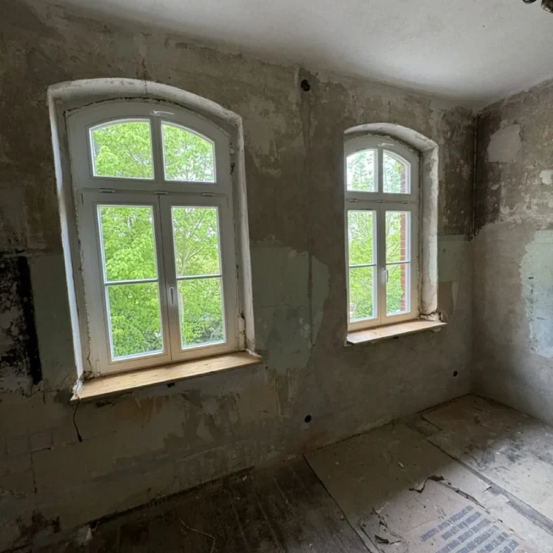 Zwei weiße Holzfenster in renovierungsbedürftigem Raum, bieten stilvolle Lichtquelle und Isolierung von NORTA.