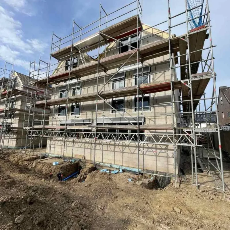 Neubau eines Doppelhauses mit Baugerüst in Köln. NORTA liefert hochwertige Fensterlösungen für moderne Bauprojekte.