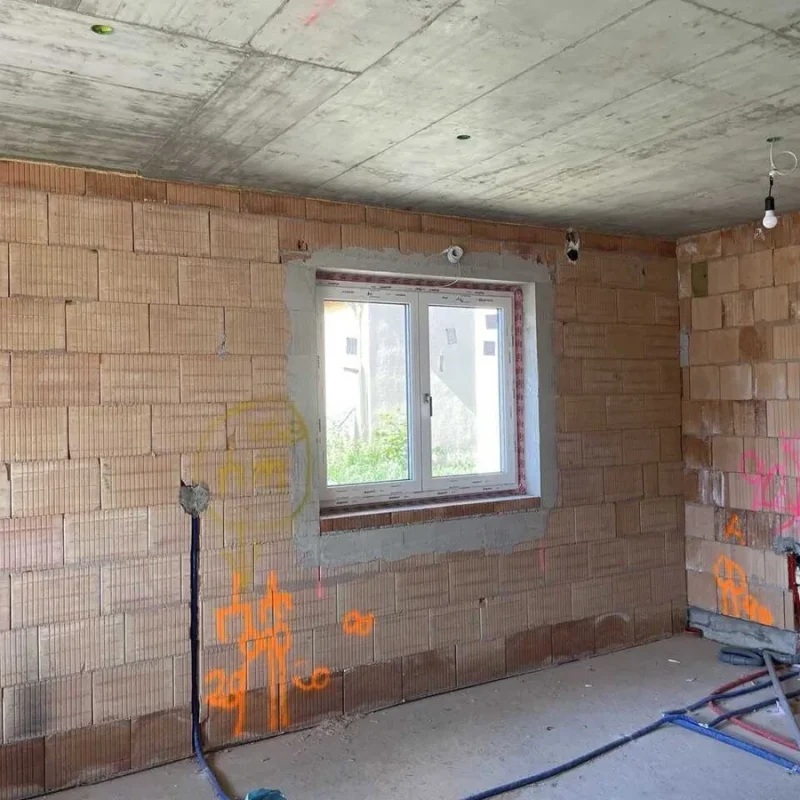 Rohbau eines Einfamilienhauses mit Fenster von NORTA. Die unvollständige Wand zeigt Baufortschritt und Installationspläne.